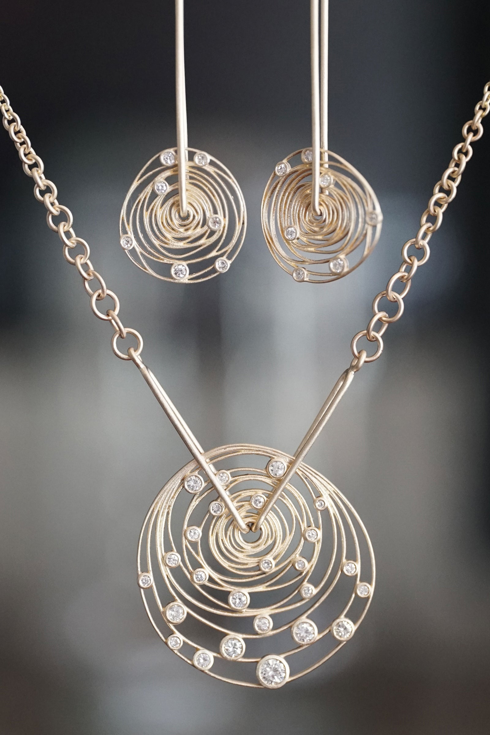 a set of yellow gold and diamond earrings and necklace in front of a grey blurred background