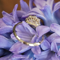 a yellow gold ring featuring a rose cut opal center stone in an 8 prong setting and with a floral diamond halo rotated to show the backside basket design