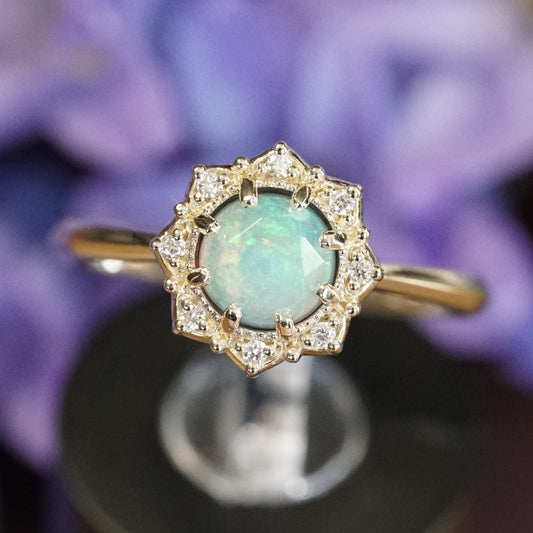 a macro photo of a yellow gold ring featuring a rose cut opal center stone in an 8 prong setting and with a floral diamond halo