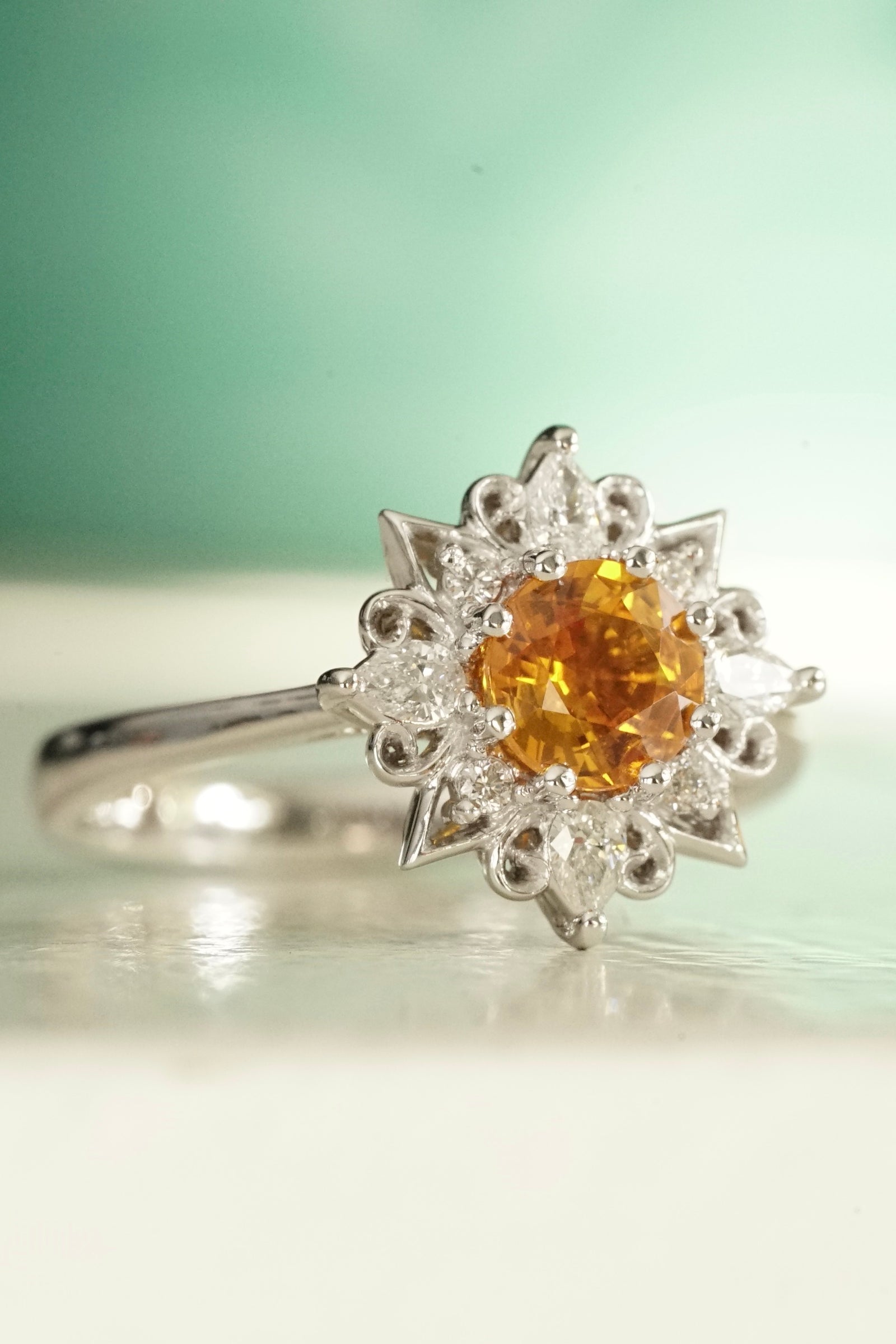 a white gold diamond and orange sapphire engagement ring on a shiny white surface