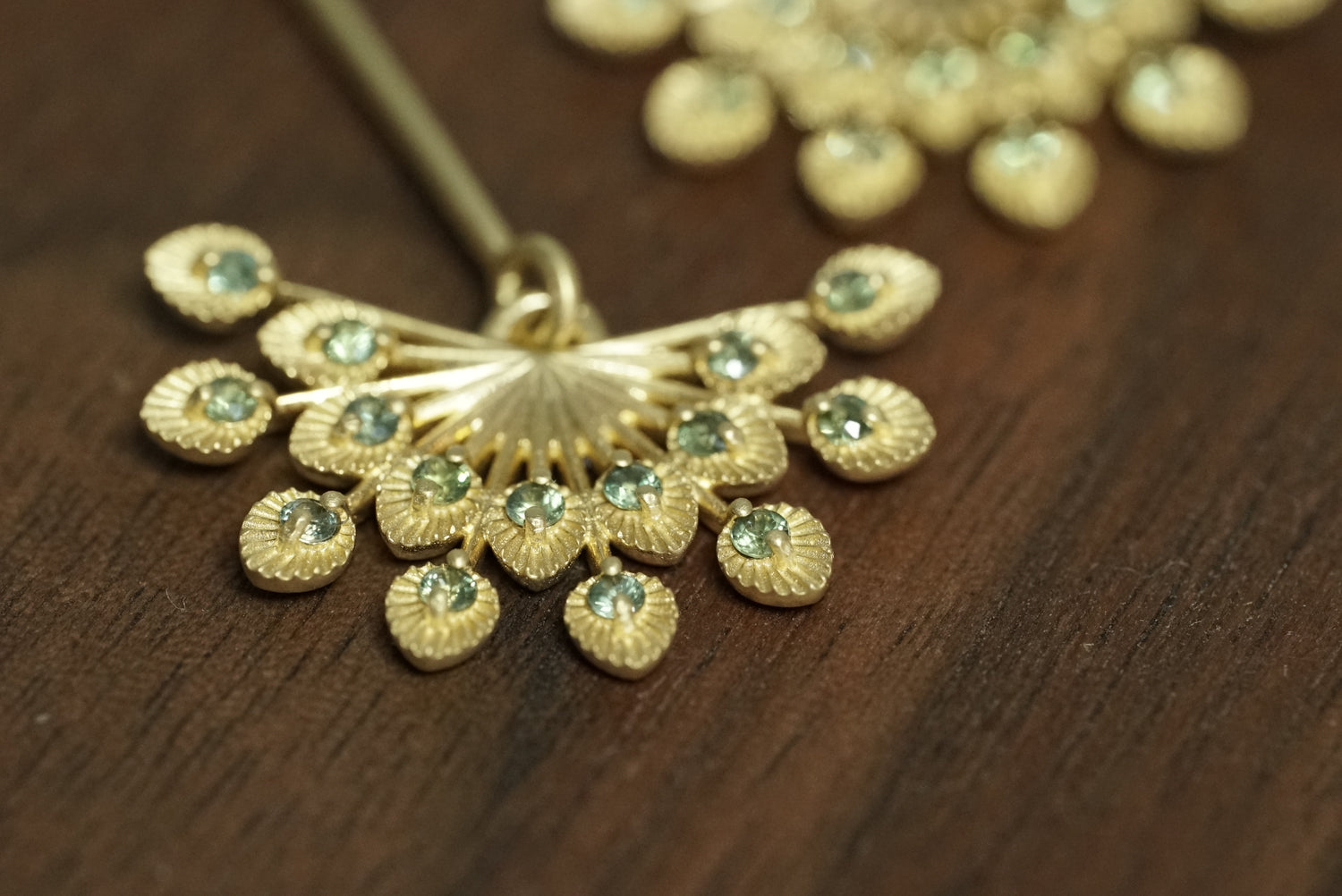 a macro photo of a pair of 14k yellow gold and teal sapphire drop earrings on a wood background