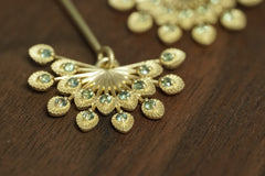 a macro photo of a pair of 14k yellow gold and teal sapphire drop earrings on a wood background
