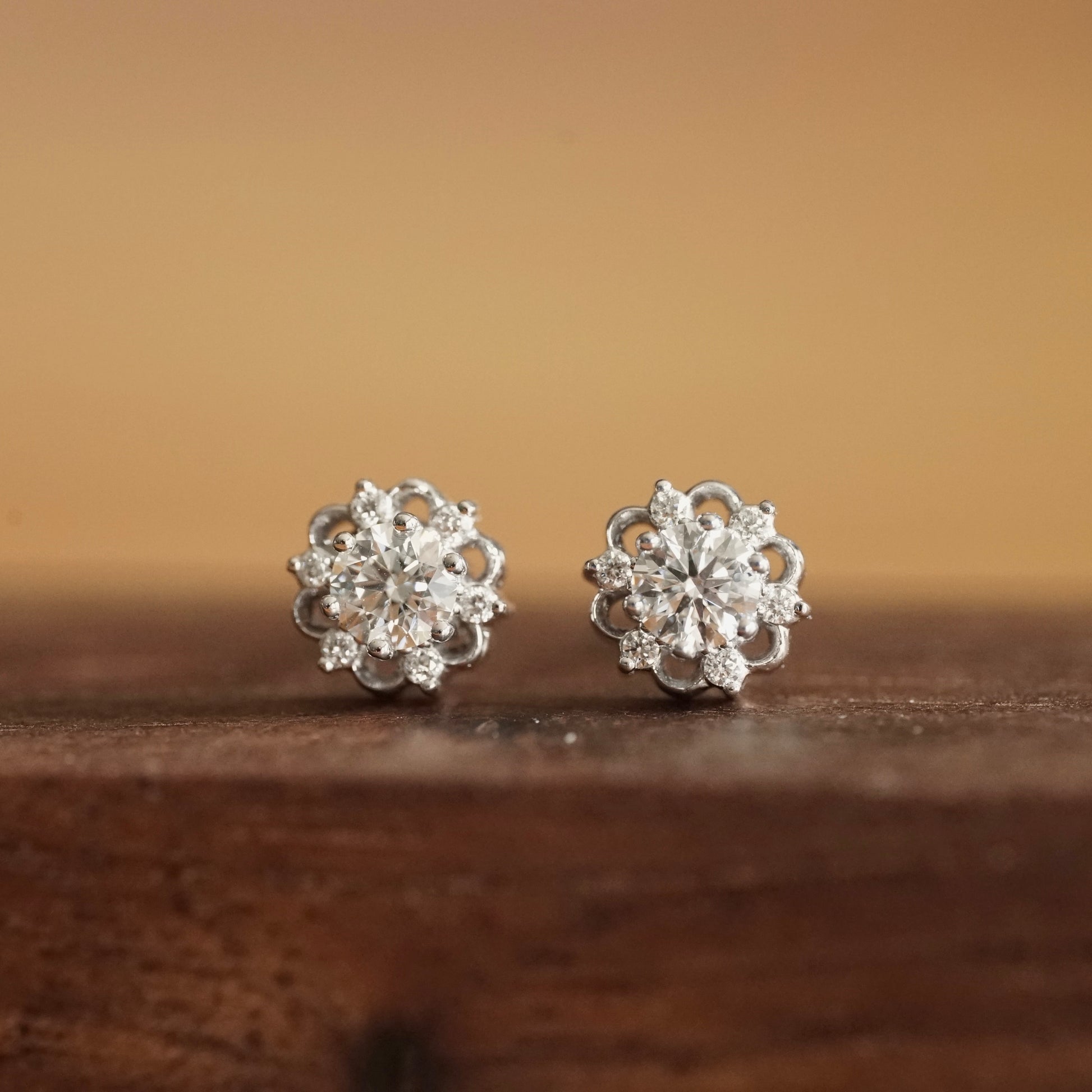 a pair of white gold stud earrings with a lab ground diamond center stone and 6 natural diamond accents rests on a wood base