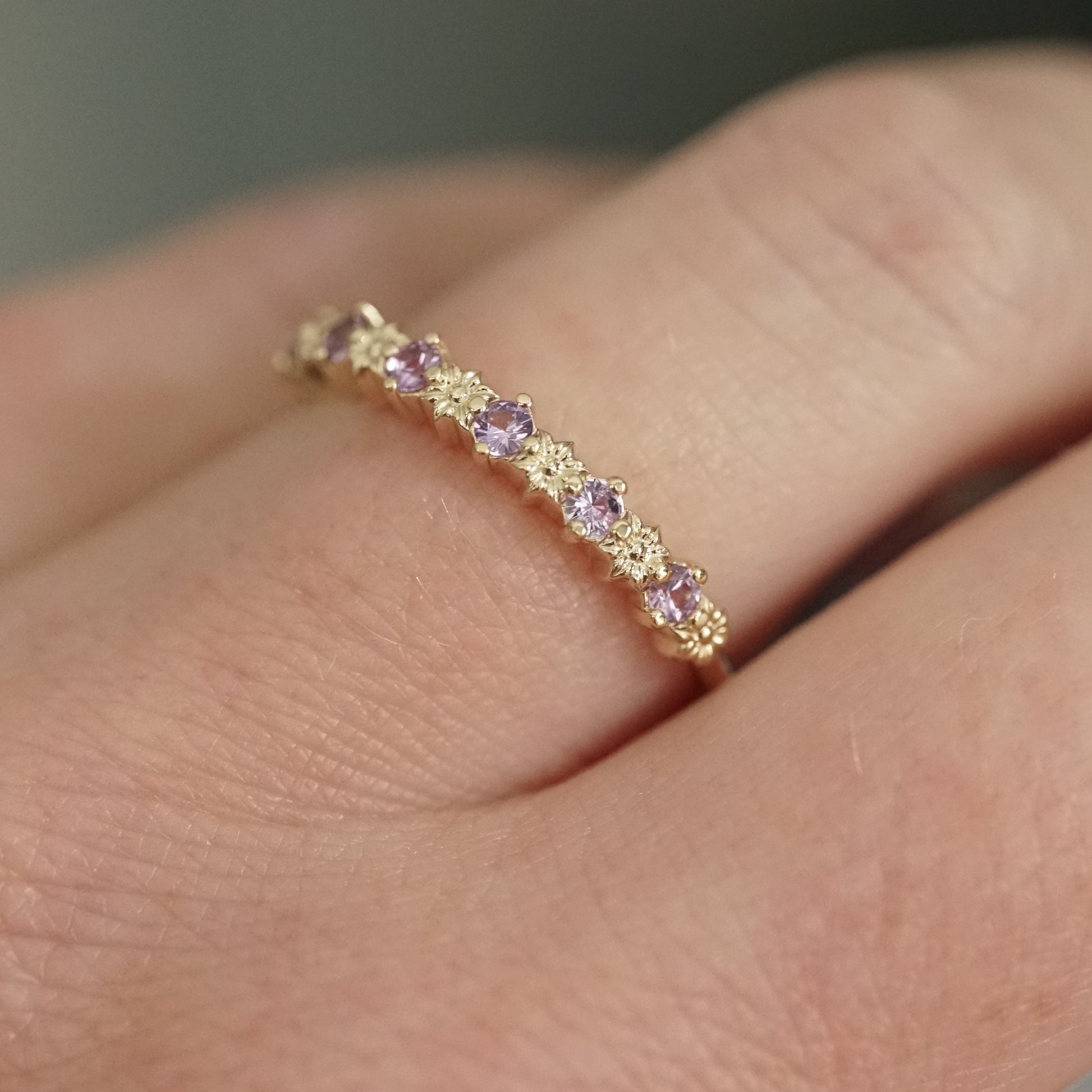 a yellow gold ring with 6 carved flowers and 5 light purple sapphires on a light skinned left hand