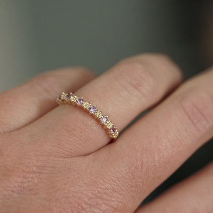 a yellow gold ring with 6 carved flowers and 5 light purple sapphires on a light skinned left hand