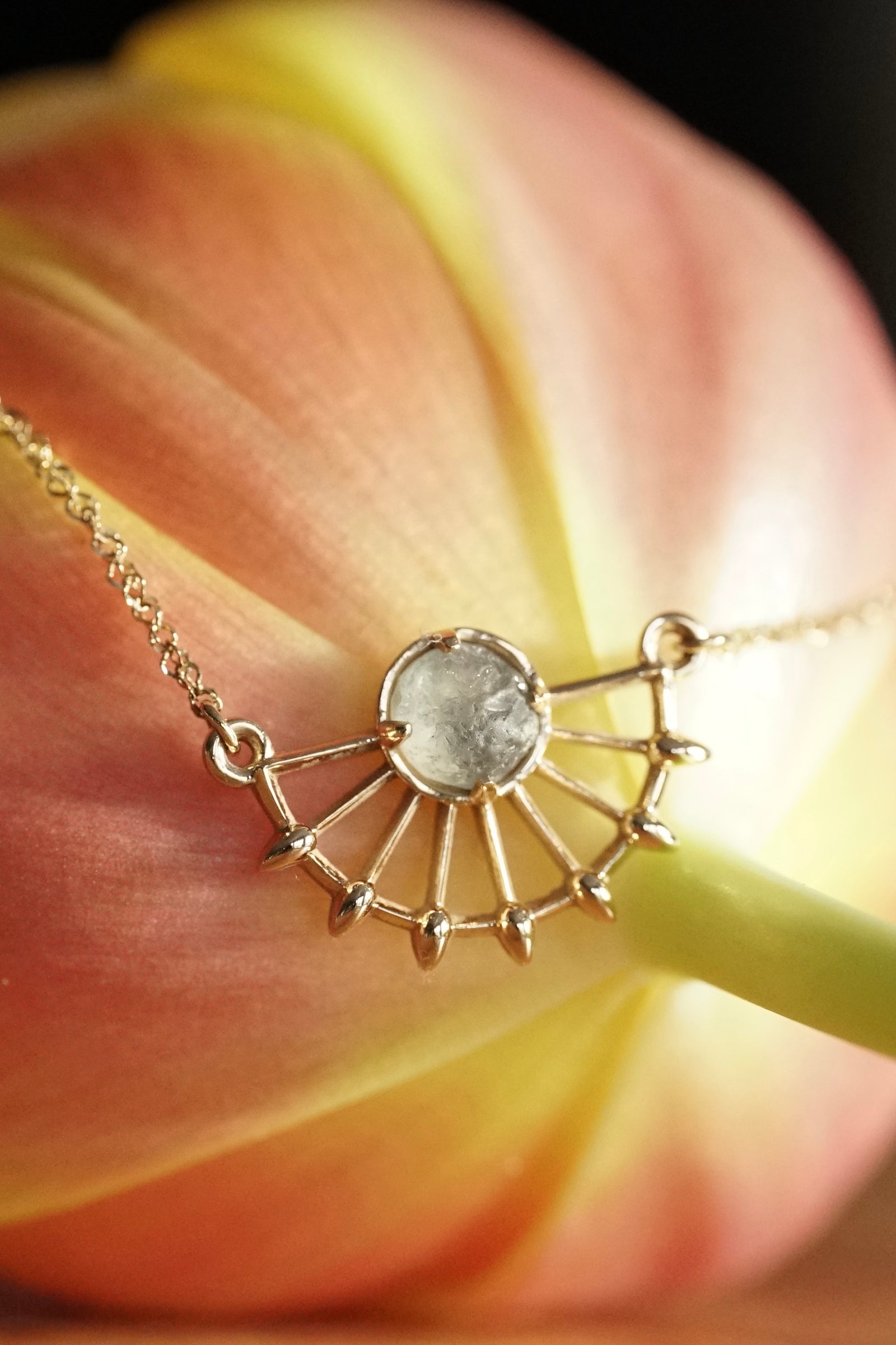 a rough sapphire set in a yellow gold pendant rests on the back of a tulip
