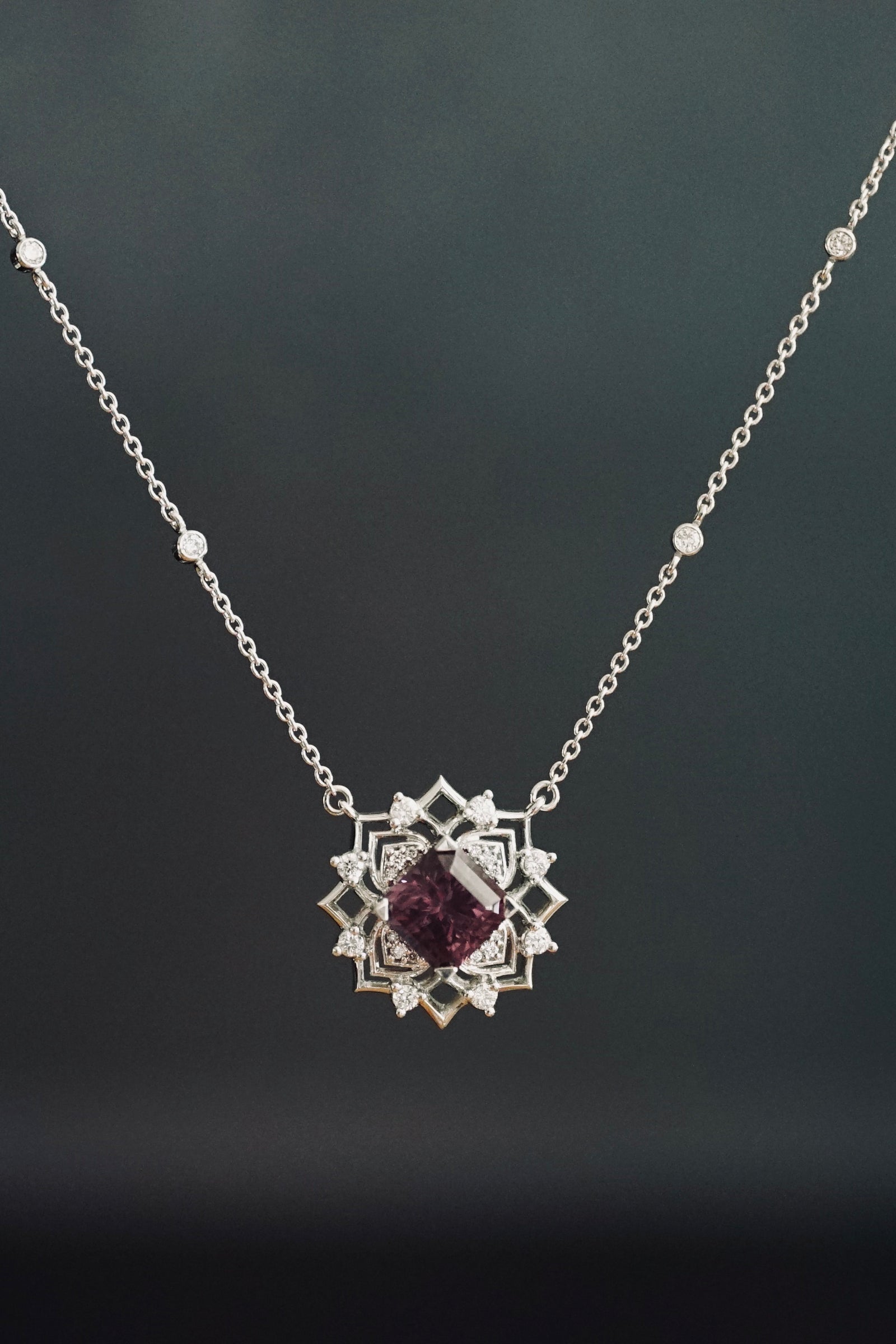 a white gold diamond and purple spinel pendant in a dark grey room
