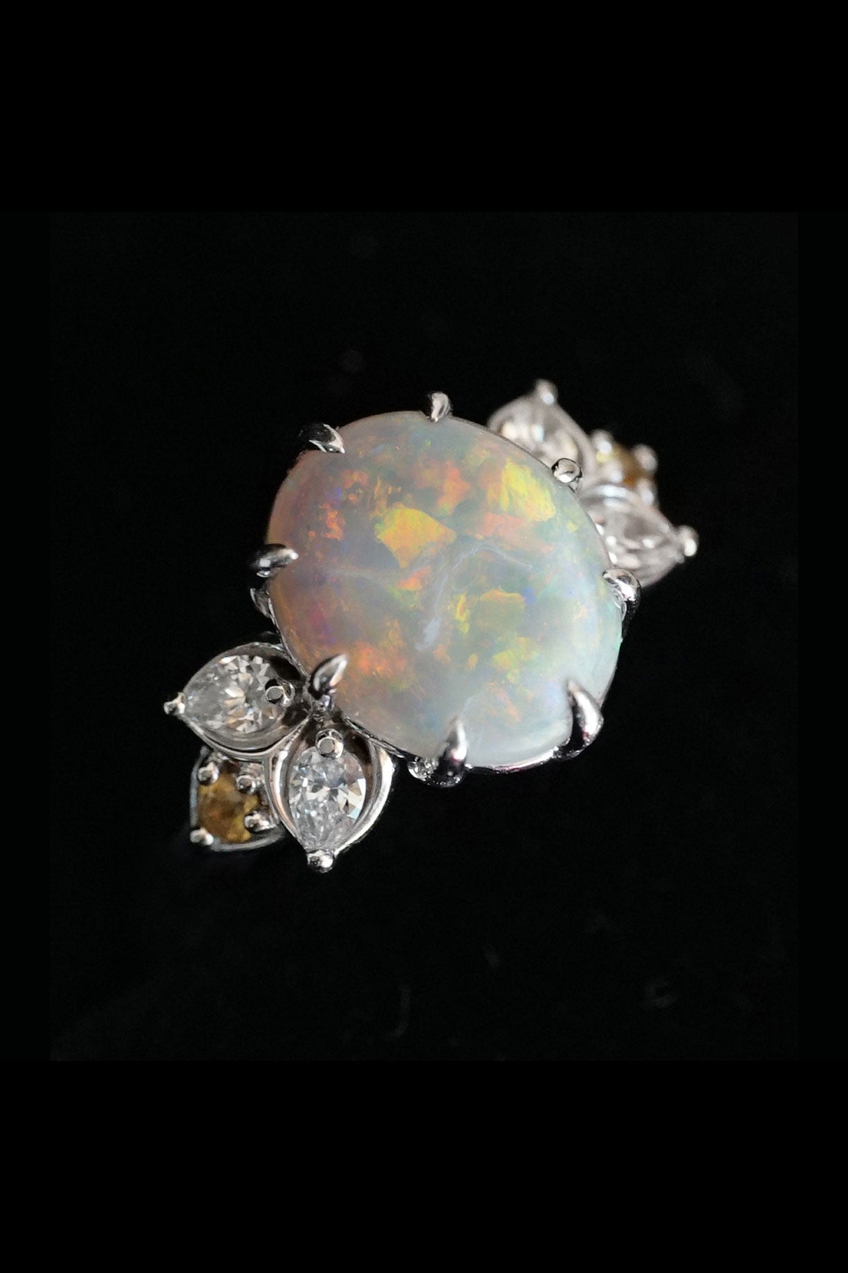 a white gold opal diamond and citrine ring on a black background