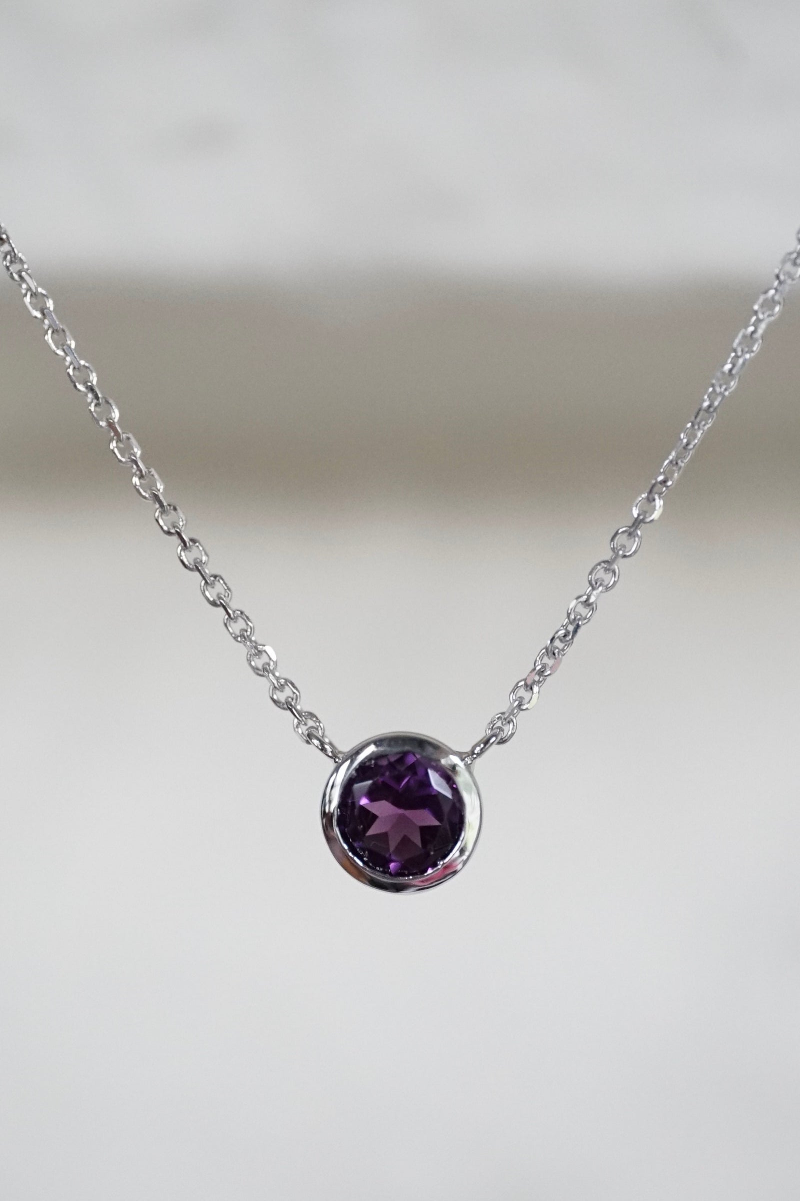 a white gold and amethyst pendant in front of a white wall