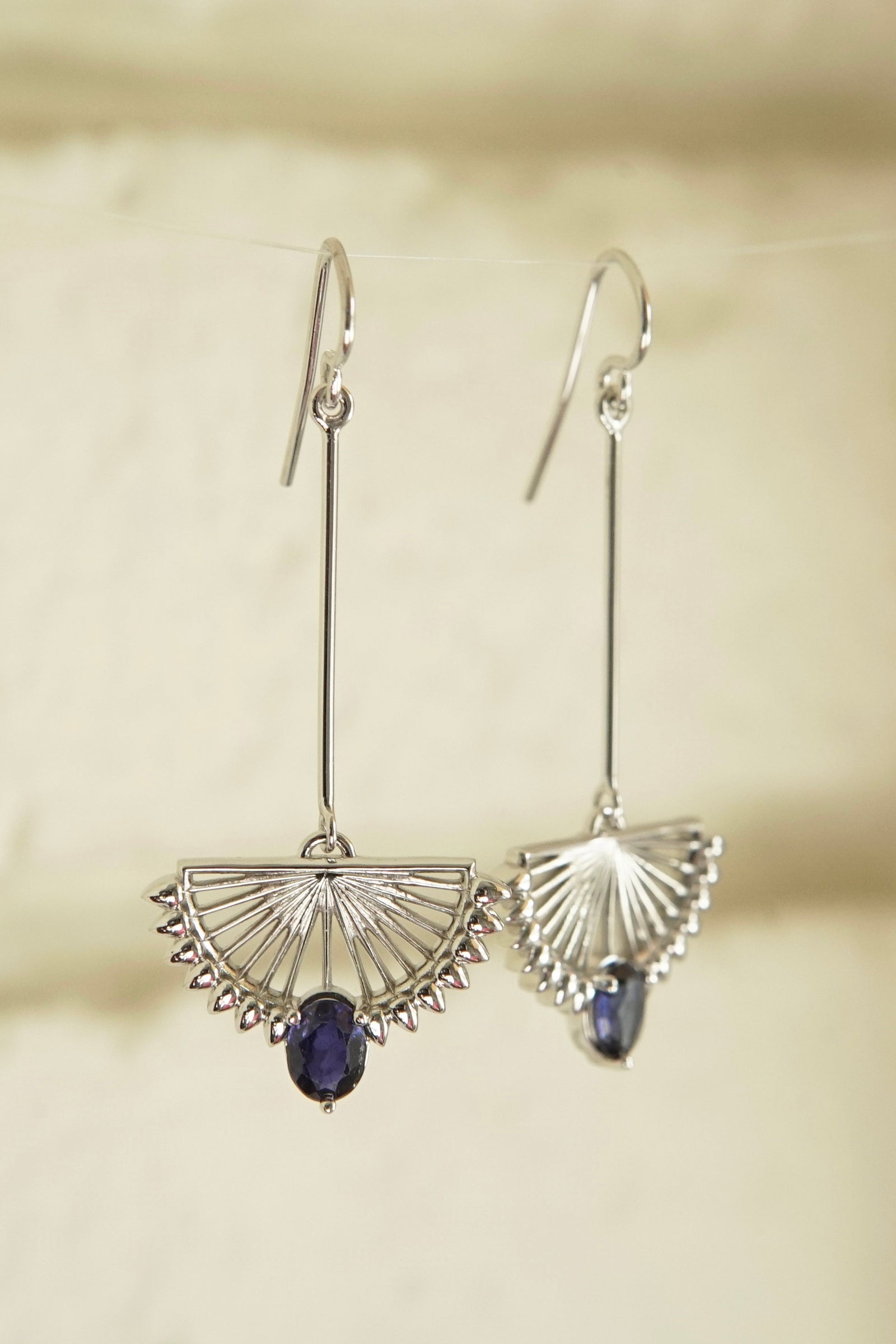 a pair of white gold and blue sapphire drop earrings in front of an off white brick wall