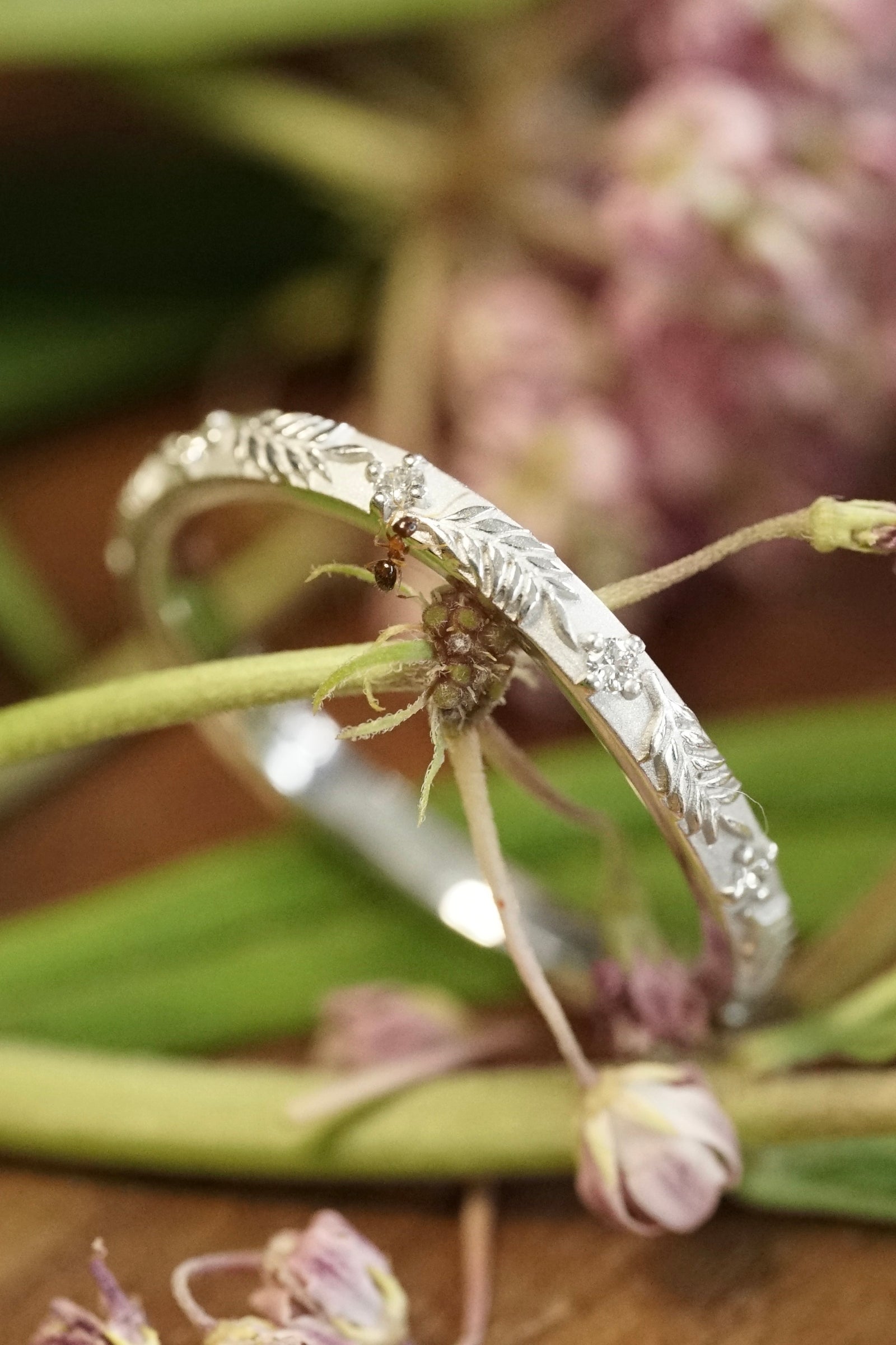 a white gold wedding band in front of flowers with a small ant stopping by for a visit