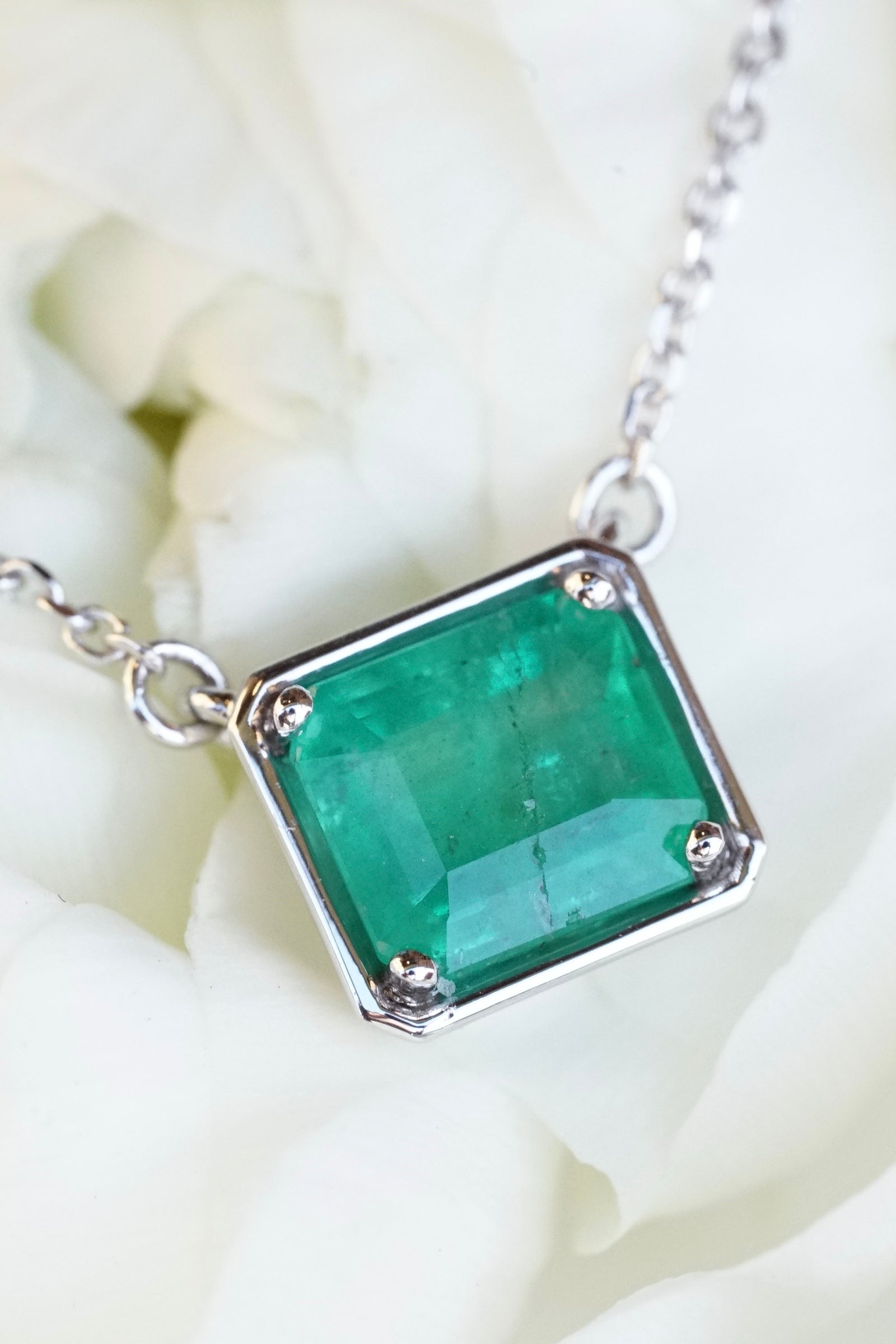 a white gold and emerald pendant on a white flower petal