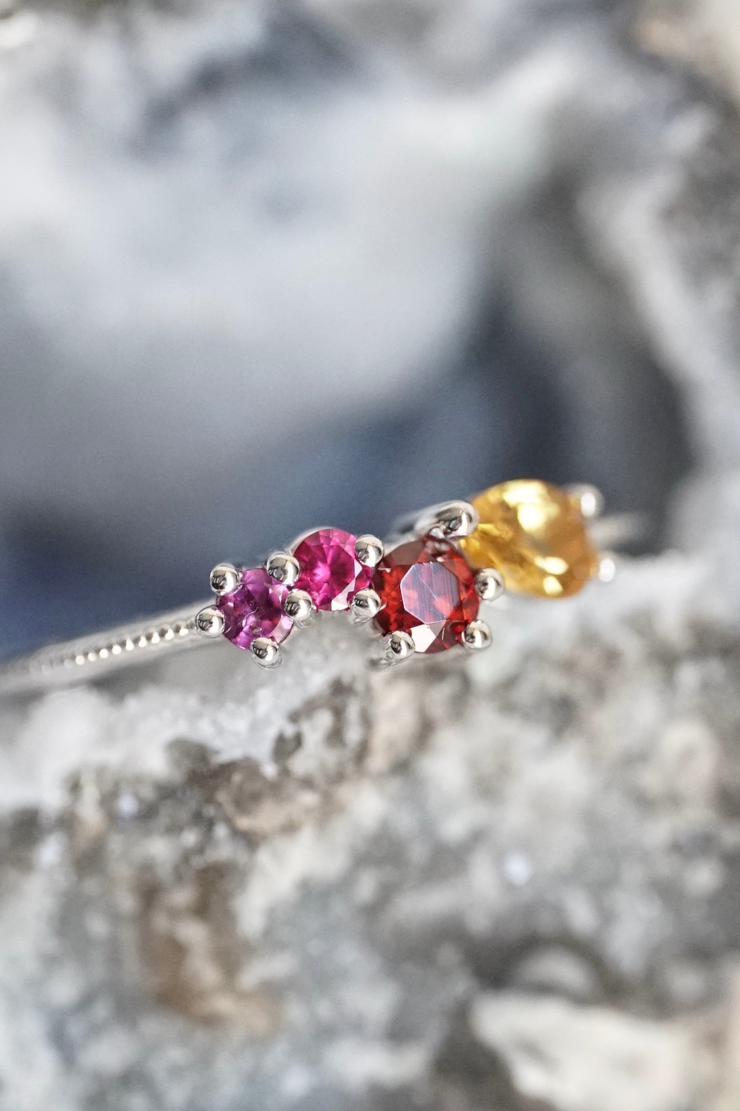 a white gold ring with pink red and yellow gems rests in a geode