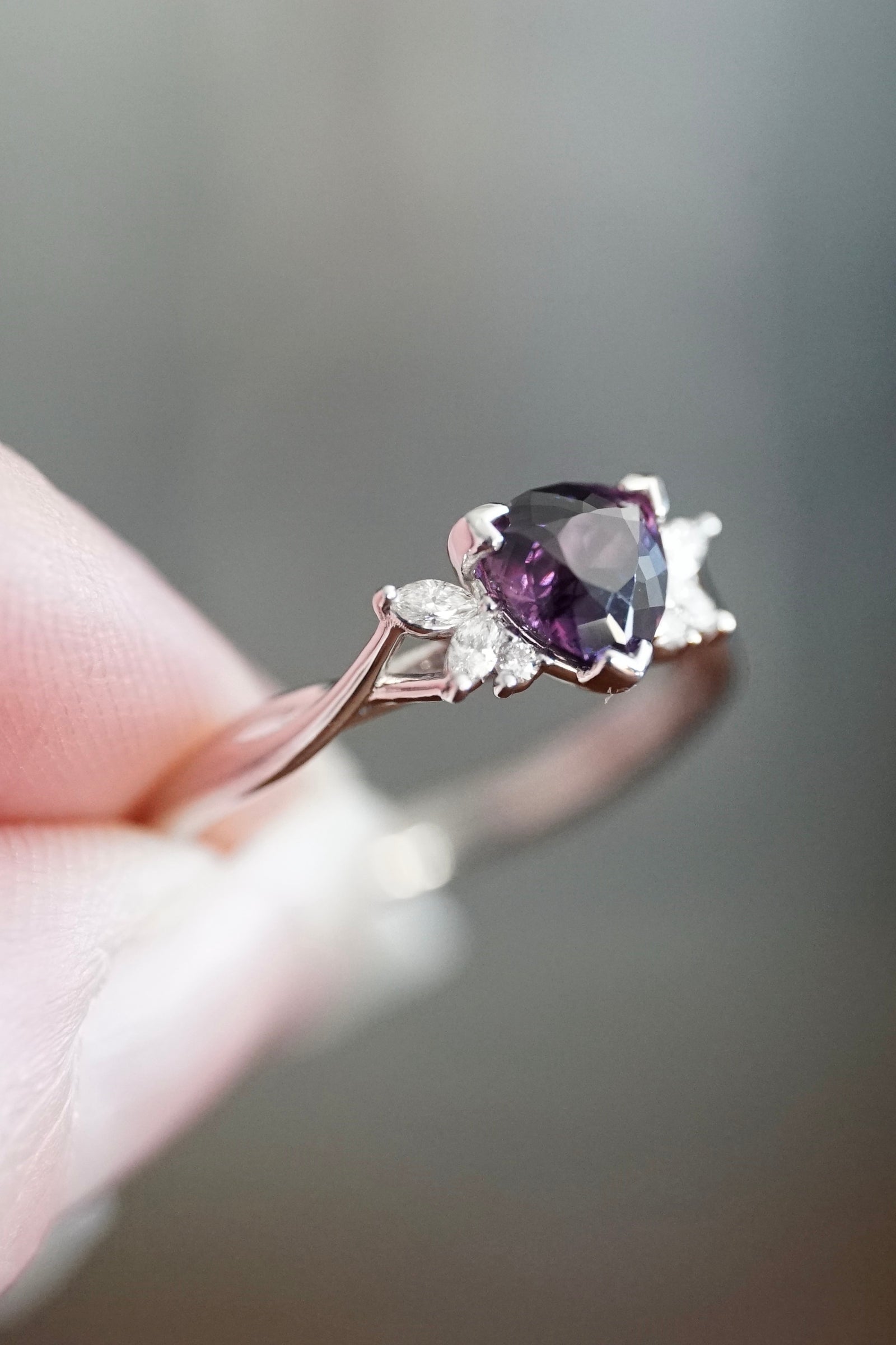 a white gold purple sapphire and diamond ring held in a light skin tone hand