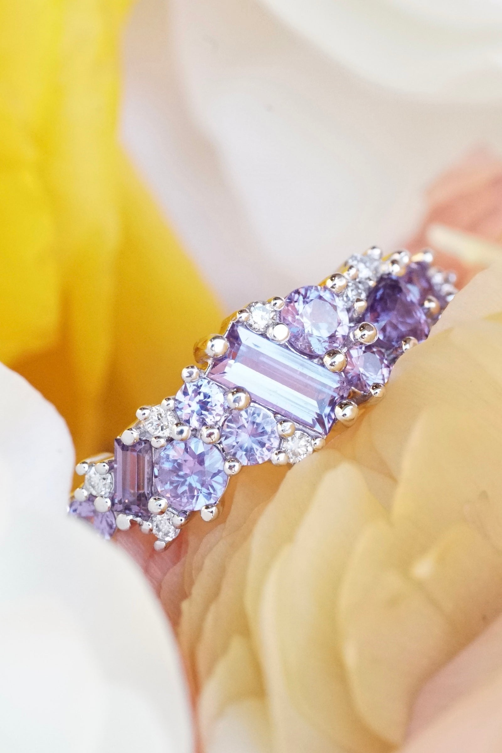 a white gold, purple sapphire, and diamond ring rests in yellow and white flowers