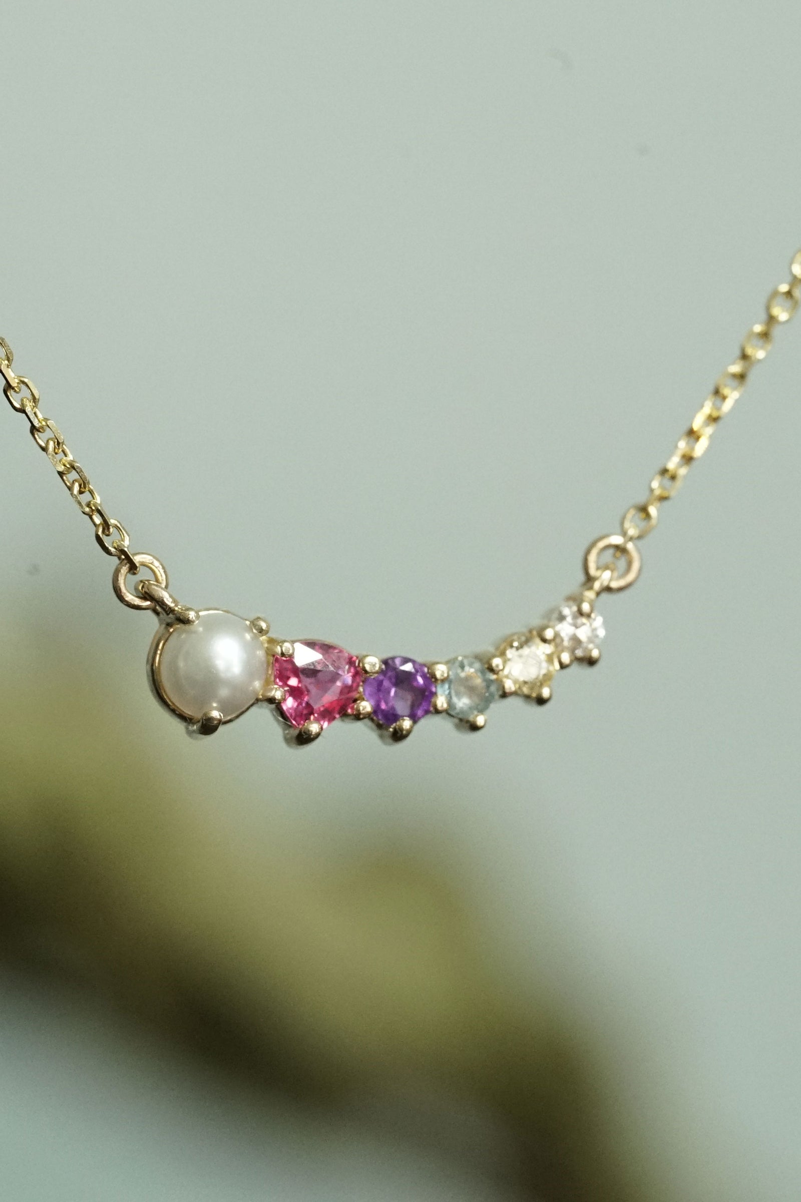 a yellow gold and multi color gem pendant in front of a light blue and green background