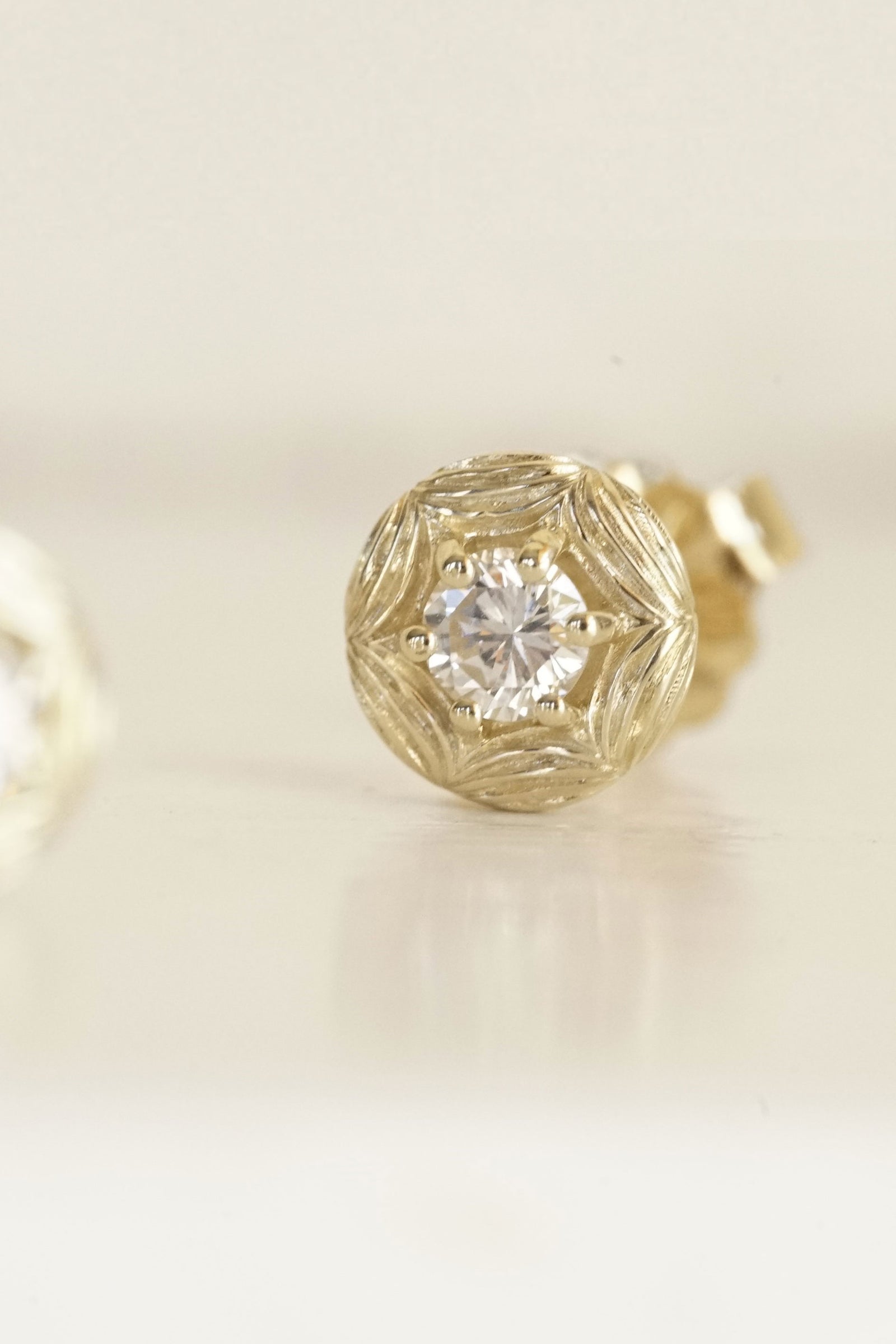 a yellow gold and diamond stud earring on a white shiny base