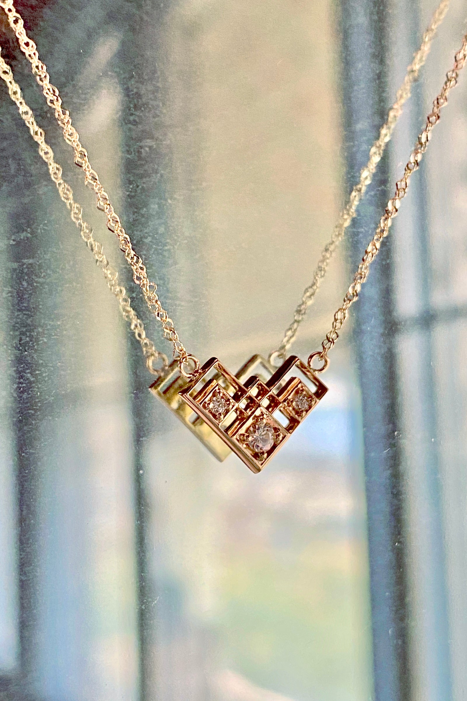 a white gold and diamond pendant suspended in front of a mirror on a sunny afternoon