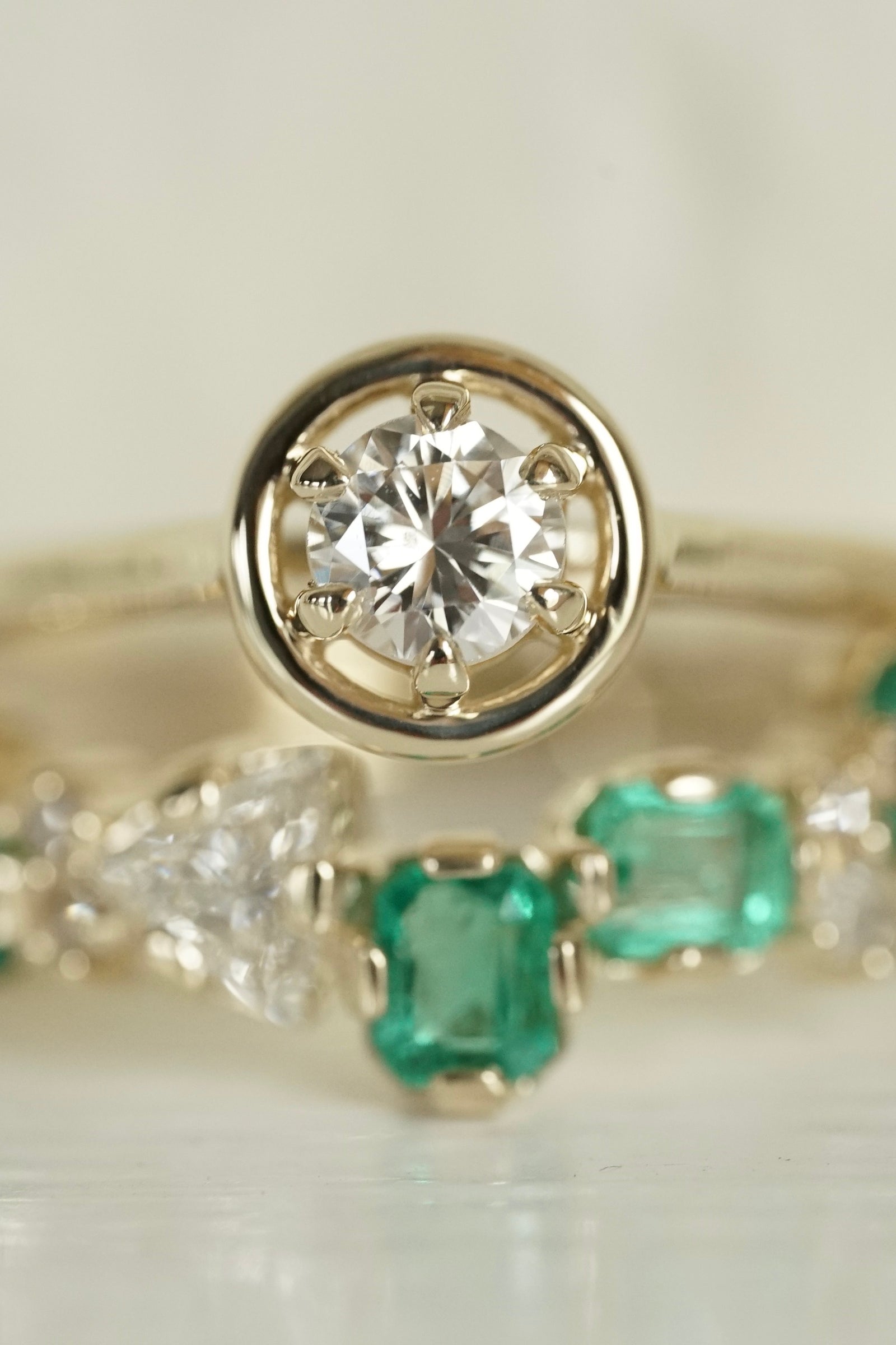 a yellow gold and diamond ring in focus over a blurred emerald and diamond ring