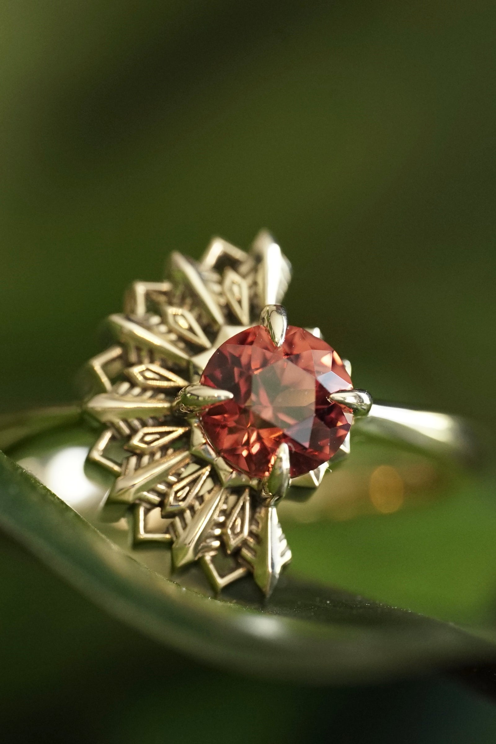 a yellow gold and garnet ring with an art deco design on a green background