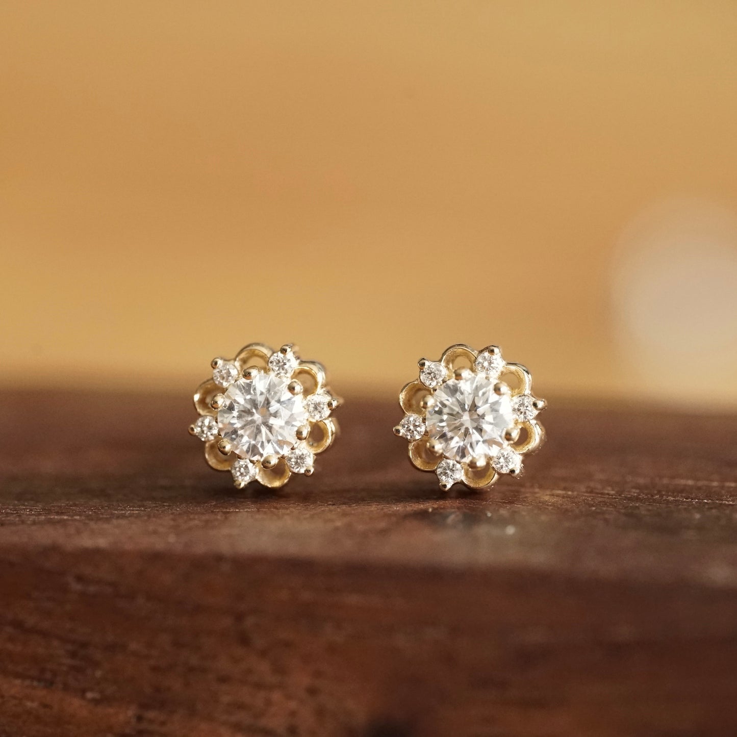 a pair of yellow gold stud earrings with a lab ground diamond center stone and 6 natural diamond accents rests on a wood base