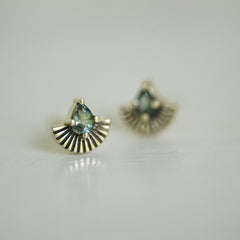 a pair of yellow gold earrings with pear shape green sapphires and fan shapes underneath on a white background