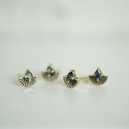 2 pairs of yellow gold earrings, one with pear shape green sapphires and one with pear shape teal sapphires and fan shapes underneath on a white background