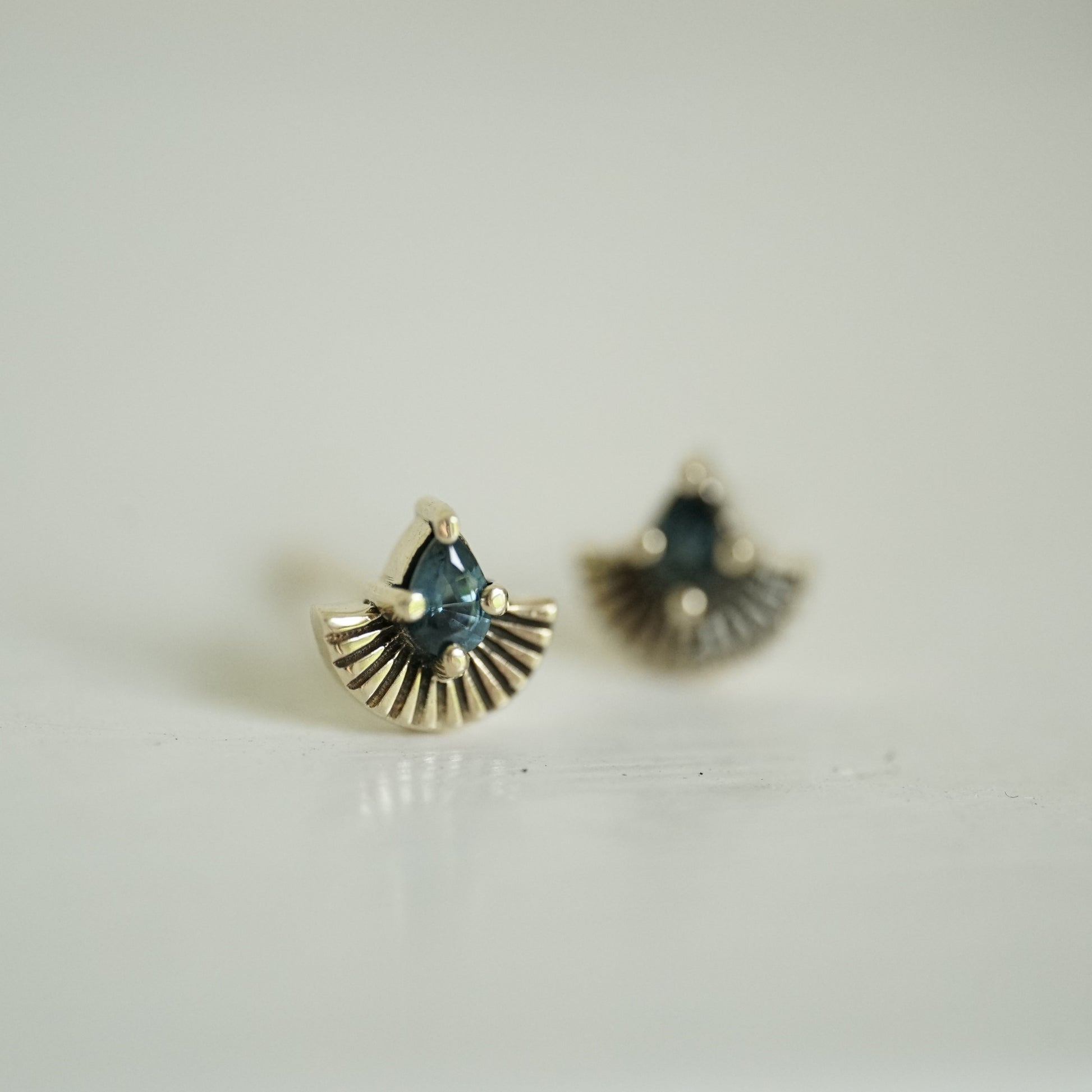 a pair of yellow gold earrings with pear shape teal sapphires and fan shapes underneath on a white background