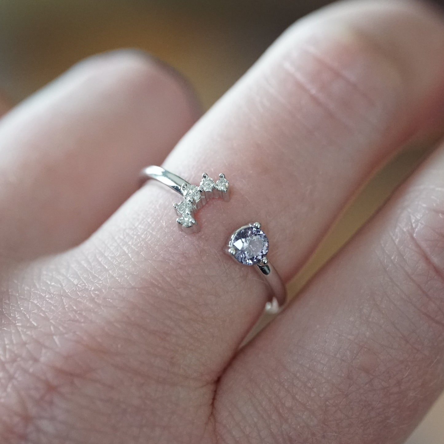 a white gold open style stacking ring with a light blue sapphire on the left and 5 diamonds on the right in a crescent shape on a light-skinned left hand