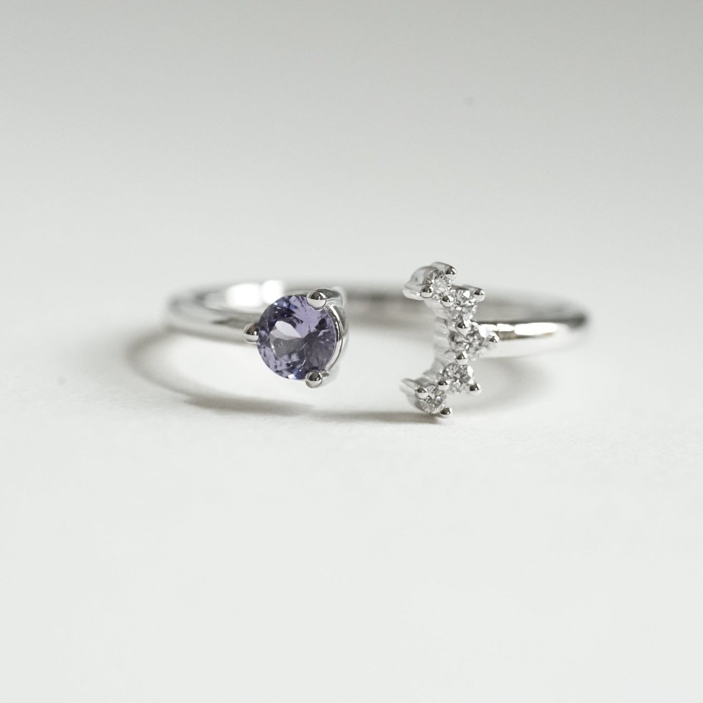 a white gold open style stacking ring with a light blue sapphire on the left and 5 diamonds on the right in a crescent shape on a white background