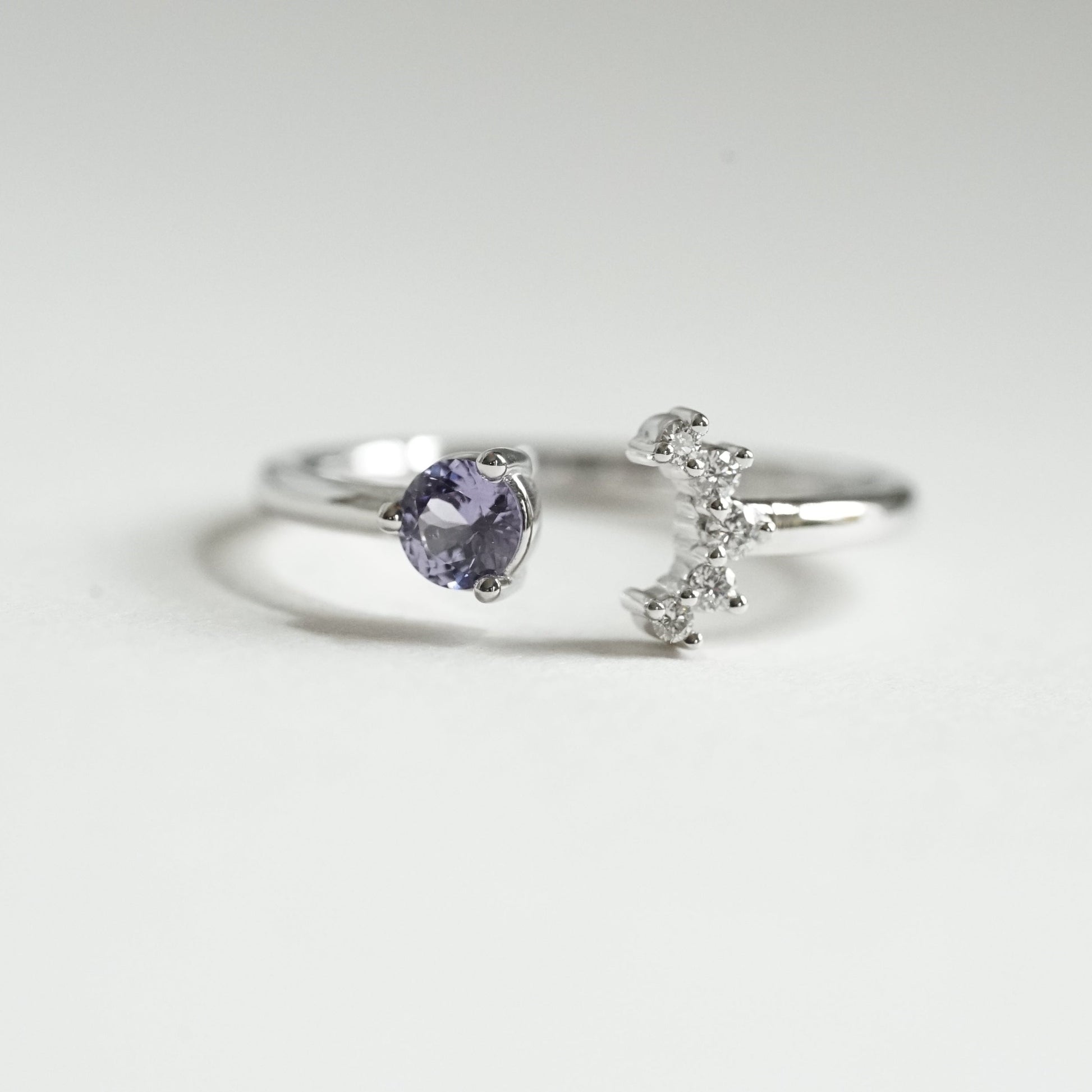 a white gold open style stacking ring with a light blue sapphire on the left and 5 diamonds on the right in a crescent shape on a white background