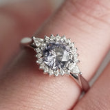 A macro photo of a lavender spinel and diamond halo style ring on a light-skinned left hand