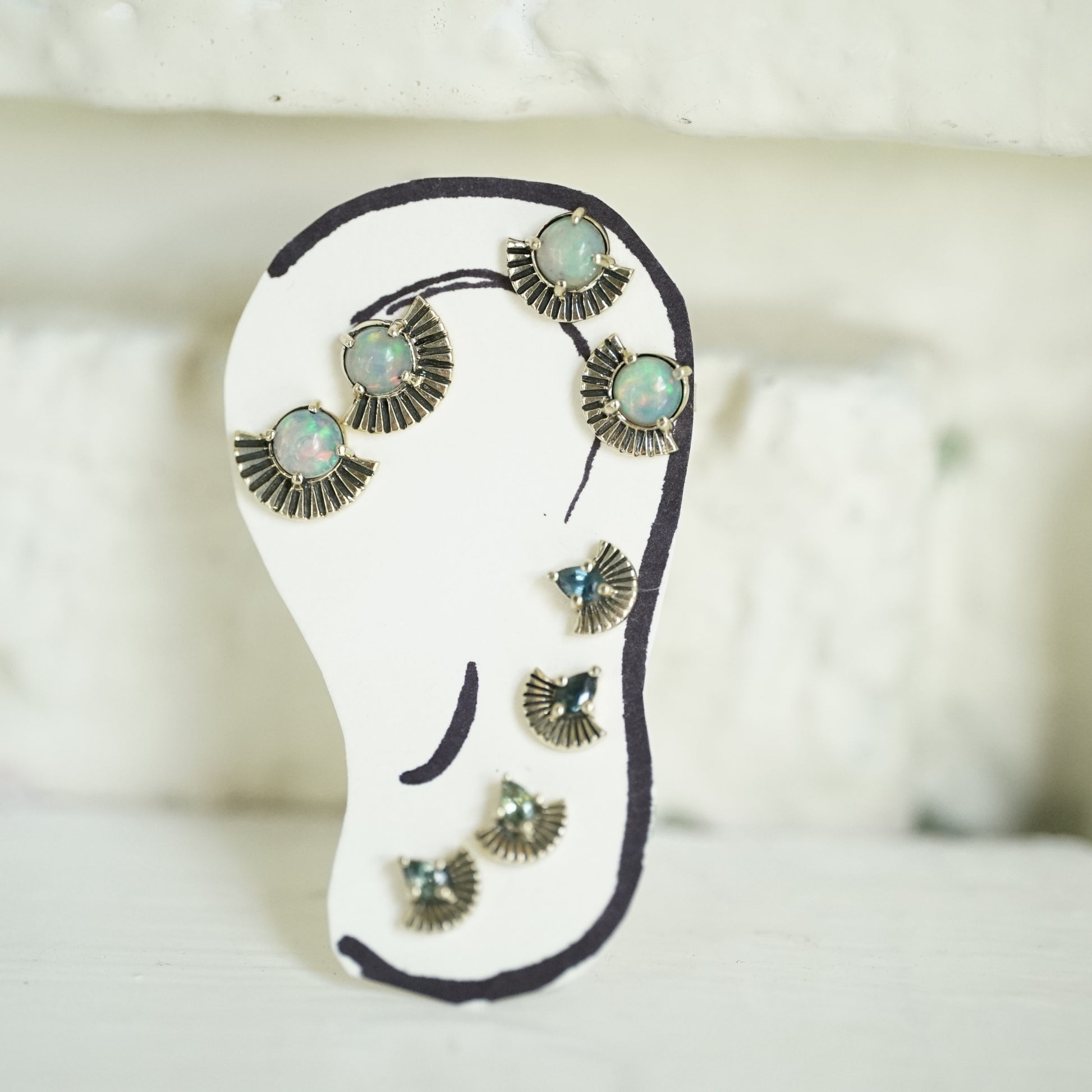 A hand drawn ear with 4 pairs of art deco inspired stud earrings, 2 pairs featuring opals and 2 pairs featuring pear shape sapphires