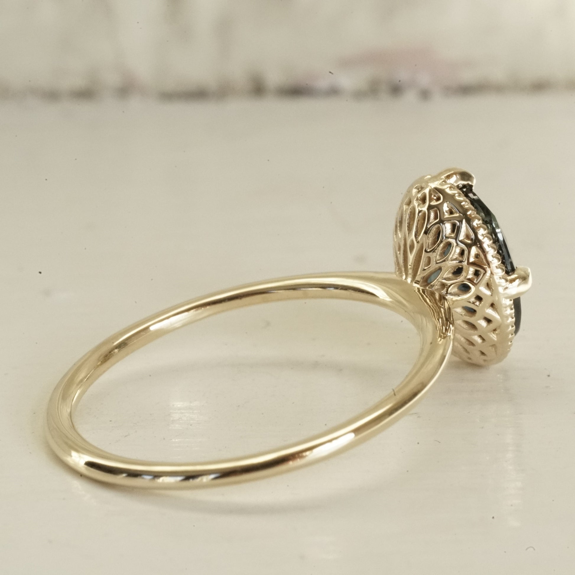 a yellow gold ring with an ornate open wirework basket on a glossy white background