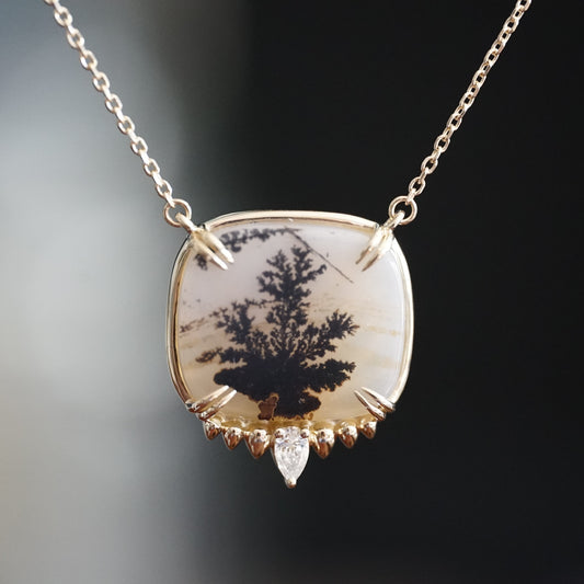 a yellow gold necklace with a dendritic agate in the center and single diamond accent at the base hangs on an open link chain