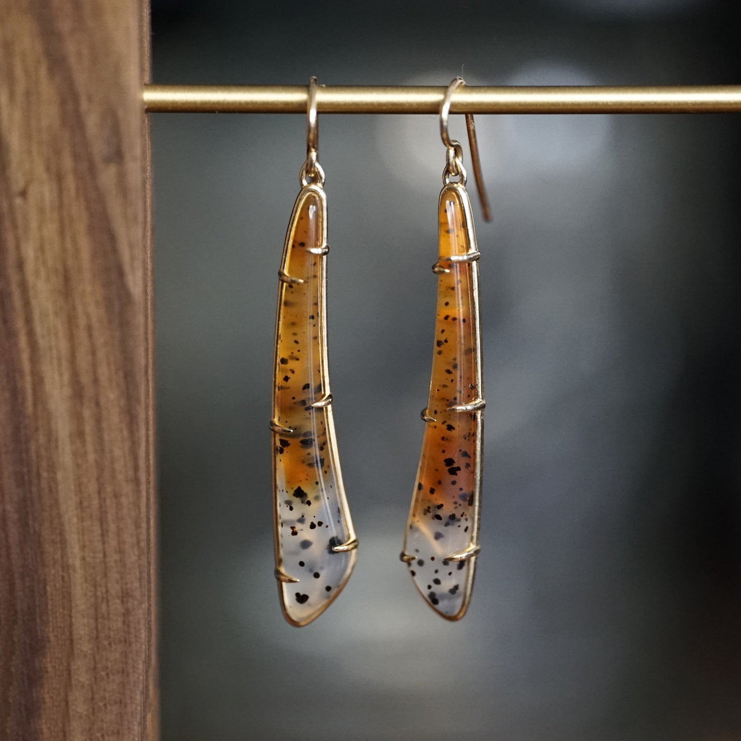 a pair of yellow gold earrings featuring elongated Montana agates which fade in color from yellow to clear and have natural black inclusions hanging on a brass bar