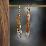 a pair of yellow gold earrings featuring elongated Montana agates which fade in color from yellow to clear and have natural black inclusions hanging on a brass bar