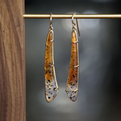 a pair of yellow gold earrings featuring elongated Montana agates which fade in color from yellow to clear and have natural black inclusions hanging on a brass bar