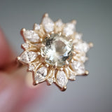 a macro photo of a yellow gold ring with a very light green center stone and mixed shape diamond halo