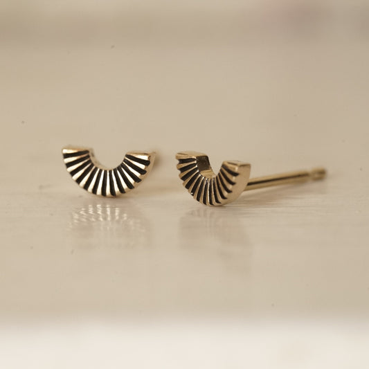 a macro photo of a yellow gold U shaped fan element stud earring on a glossy white background