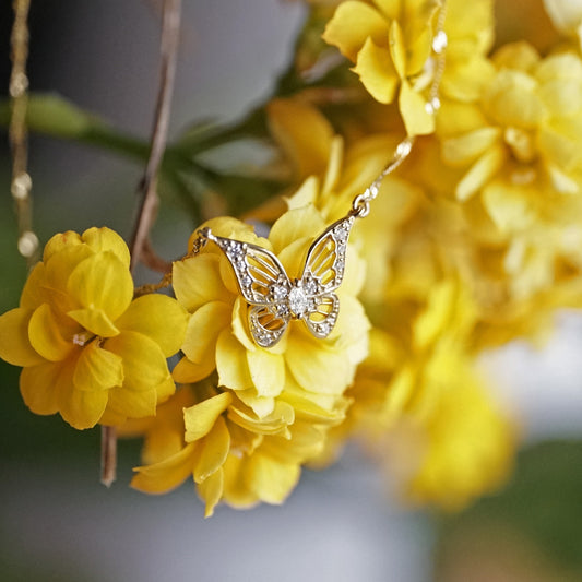 a yellow gold and diamond art deco inspired butterfly pendant on a sparkly chain laying on yellow flowers