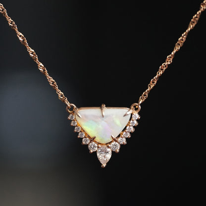 a rose gold necklace with a triangular shape opal center stone and diamond accents of graduated sizes hangs suspended