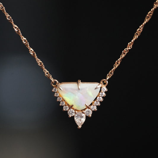 a rose gold necklace with a triangular shape opal center stone and diamond accents of graduated sizes hangs suspended