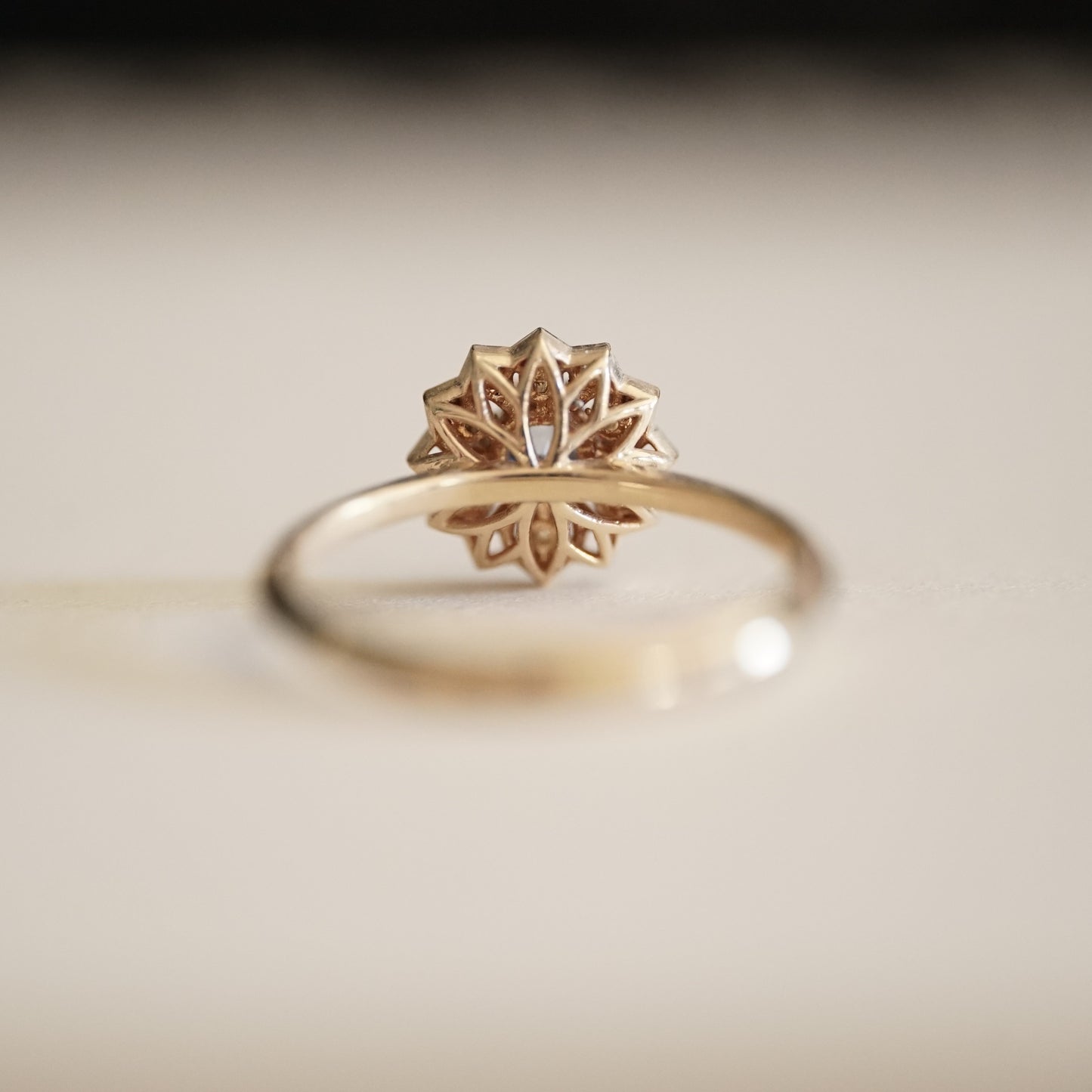 a yellow gold ring with a light blue sapphire enter stone and 6 white diamond accents in an open wire floral design rotated to show the backside view of the ring