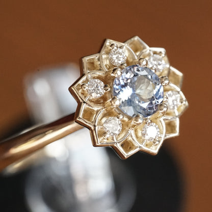 a macro photo of a yellow gold ring with a light blue sapphire enter stone and 6 white diamond accents in an open wire floral design