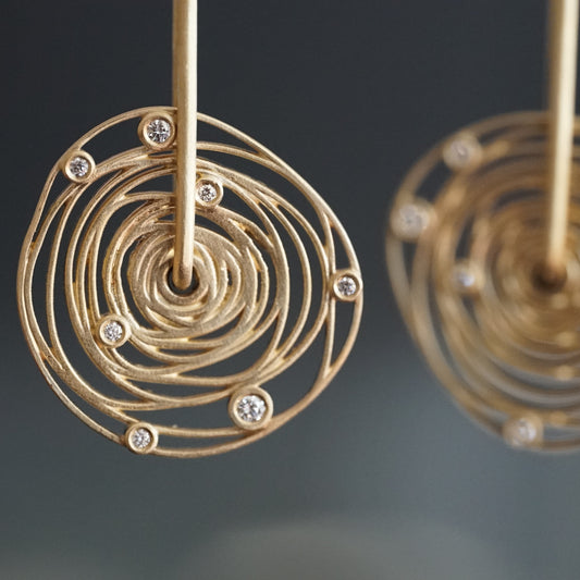 a macro photo of a 14K yellow gold and diamond earring with thin wirework loosely emulating the rotation of the planets around the sun