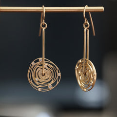 a pair of 14K yellow gold and diamond earrings with thin wirework loosely emulating the rotation of the planets around the sun hanging on a brass wire