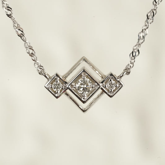 an art deco inspired white gold pendant with 3 round diamonds in squares on point attached to a sparkly white gold chain