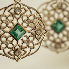 a macro photo of a yellow gold earring with princess cut emerald center stones and round and princess cut diamond earrings 
