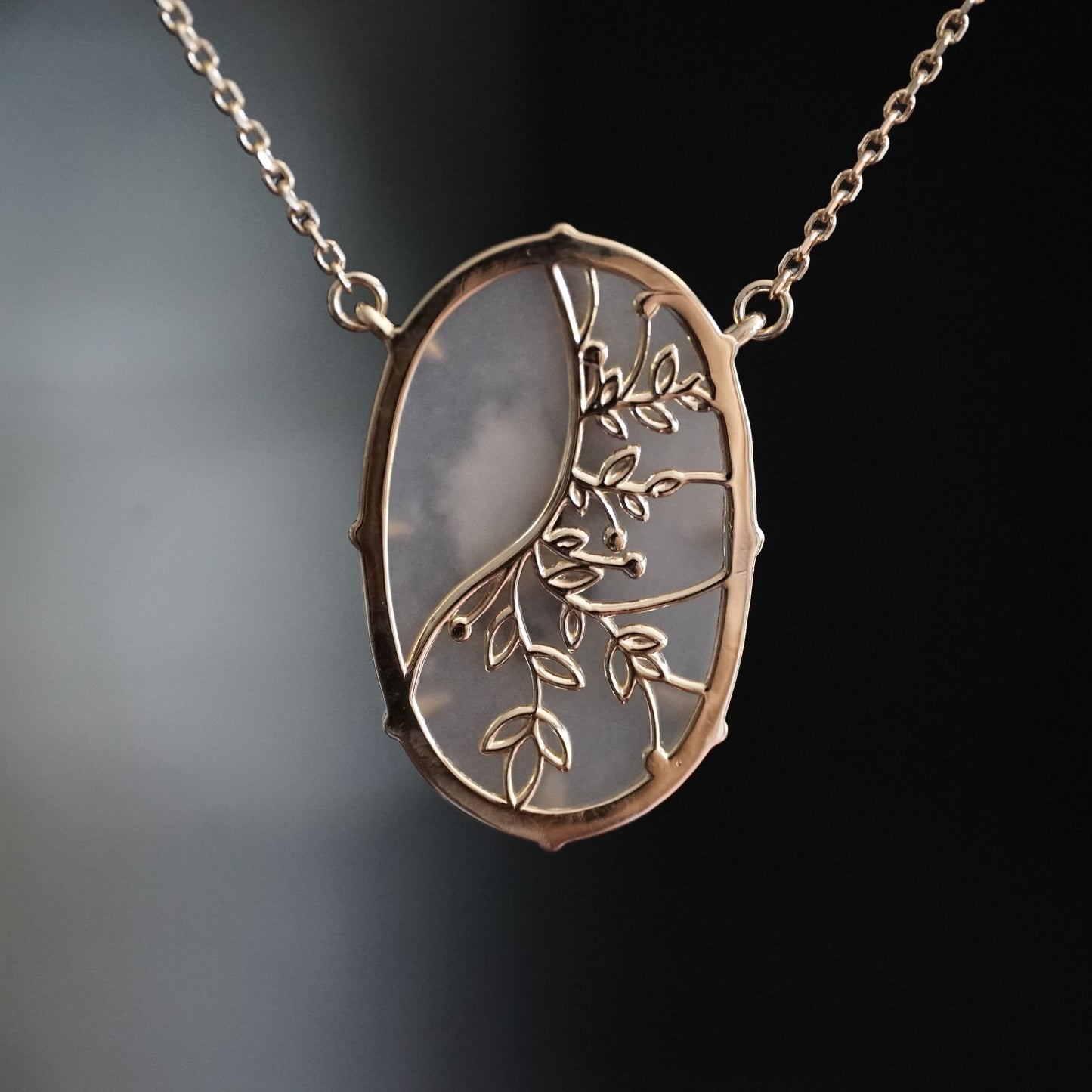 a yellow gold pendant featuring an oval dendritic agate is suspended on an open link chain rotated to show the detail floral design on the back